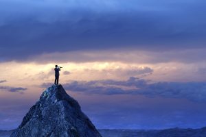 man standing on a mountain looking through a spyglass