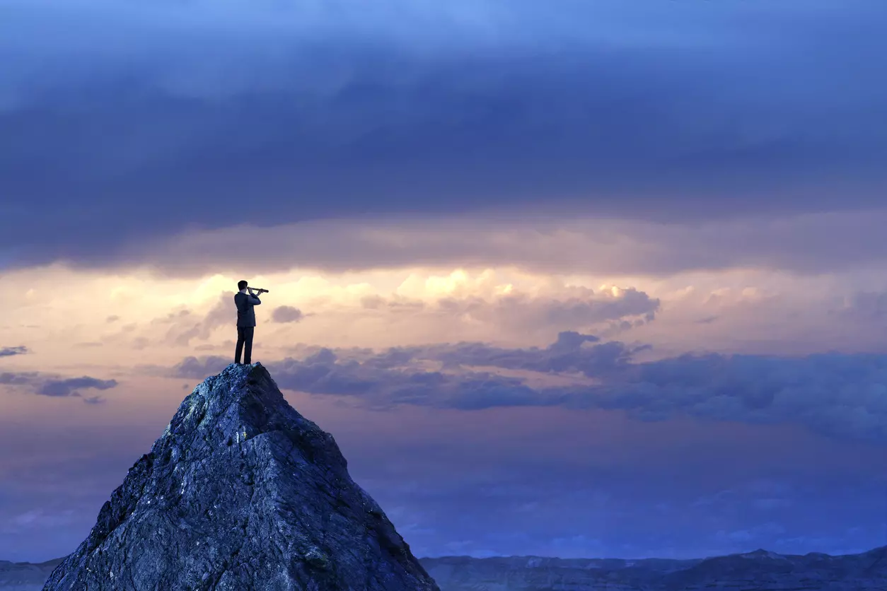 man standing on a mountain looking through a spyglass