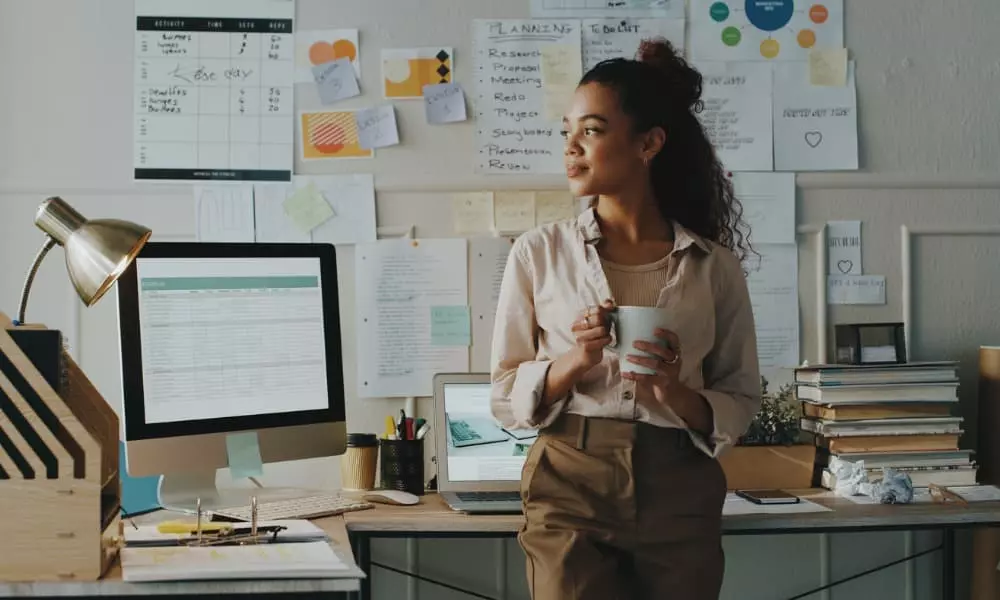 A young business entrepreneur standing in her office with her computer and notes with ideas surrounding her.