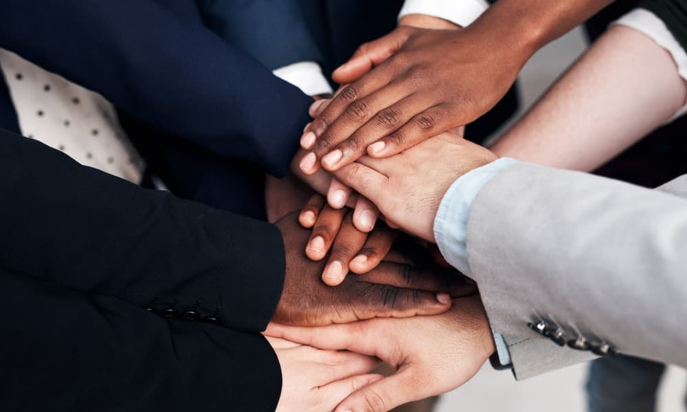 A group of diverse businesspeople stack hands in a gesture of unity.