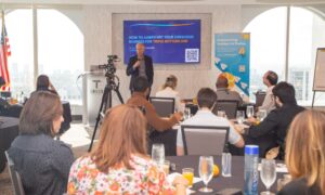 A man stands in front of a screen leading a meeting of people sitting around a table.