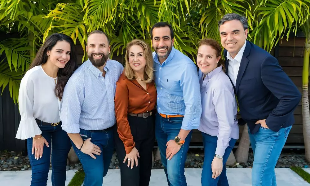 A group of smiling co-workers standing together in front of palm trees.