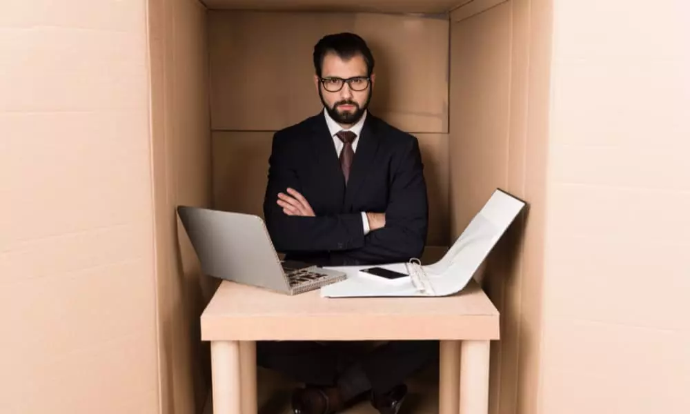 A businessman working with documents and cardboard laptop is stuck inside a small box.