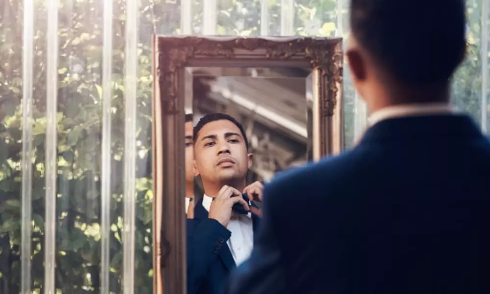 A man adjusts his tie while looking in the mirror.