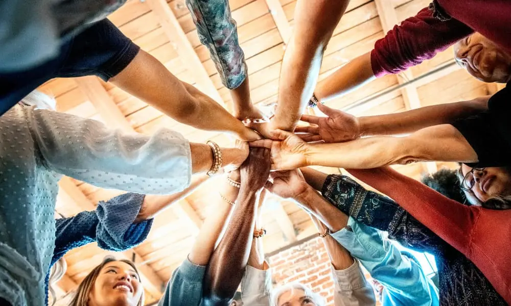 A group of people stand in a circle with their hands together in the center.