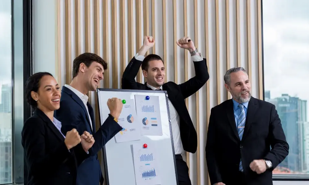 A group of employees celebrate while standing around a group of charts showing company success.