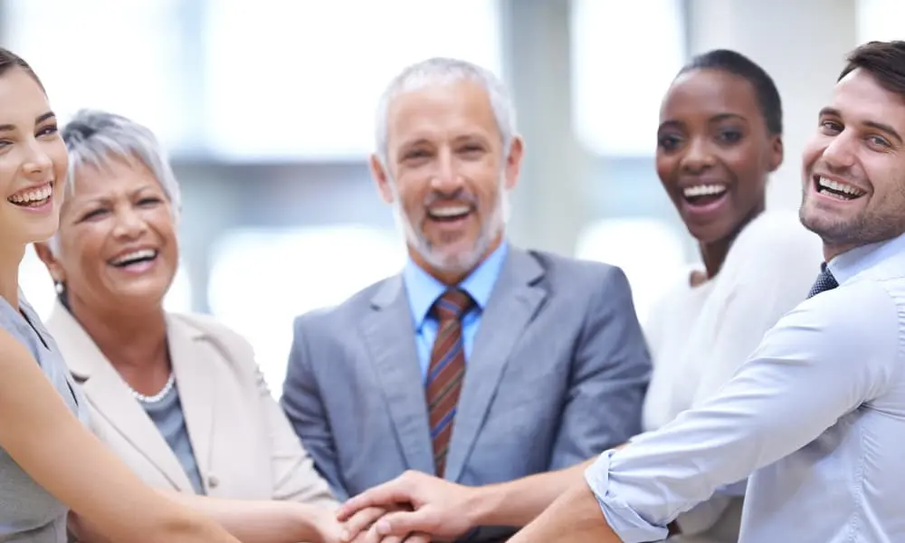 A diverse group of employees join hands in a sign of unity.