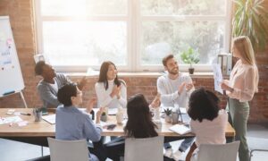 Employees sitting around a meeting table applaud a presentation by a female manager.