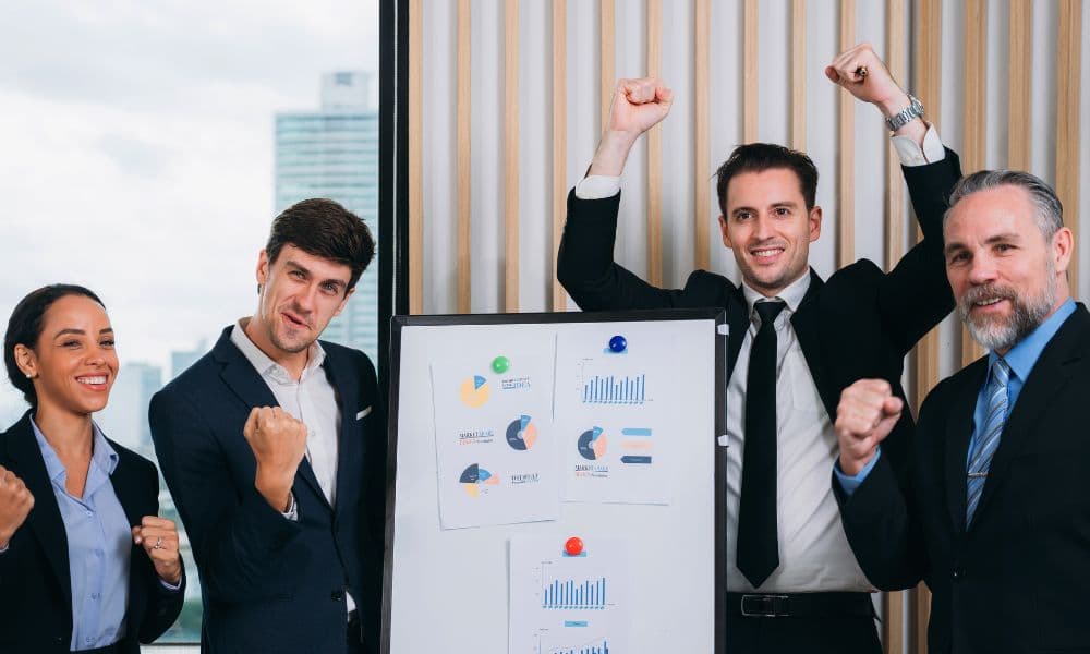 A group of excited business people around a chart showing their progress.