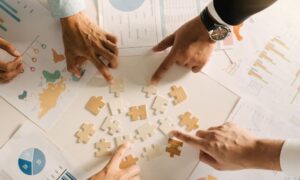 Four hands are on puzzle pieces in the midst of planning documents