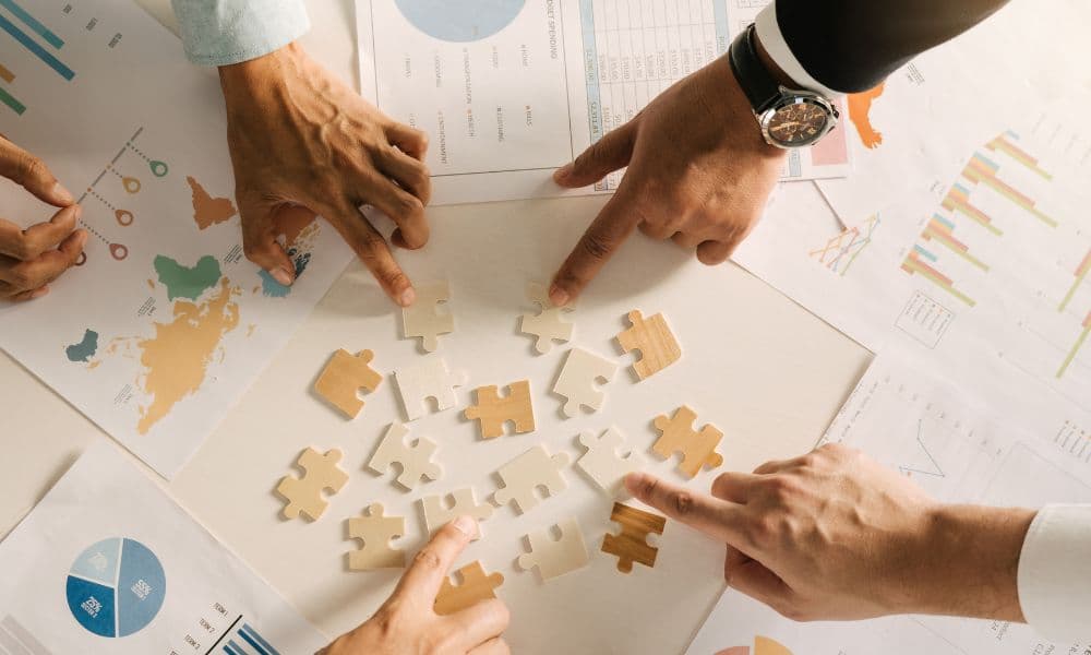 Four hands are on puzzle pieces in the midst of planning documents